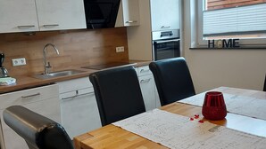 A modern kitchen with white cabinets, a black range hood, and a built-in oven. There is a dining table with chairs and a red cup on it.