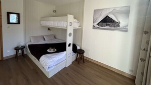 Quarto com beliche, ventilador de teto, um quadro na parede e uma mesa pequena com xícaras.