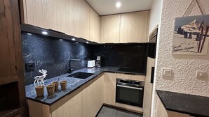 Uma cozinha compacta com armários de madeira, bancada preta, pia, cafeteira e forno pequeno.
