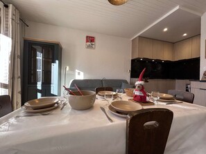 Ein Essbereich mit einem Tisch, der für vier Personen gedeckt ist, einschließlich Teller, Schüsseln und Besteck. Auf dem Tisch liegt ein Plüschtier, und an der Wand ist ein Fernseher angebracht.