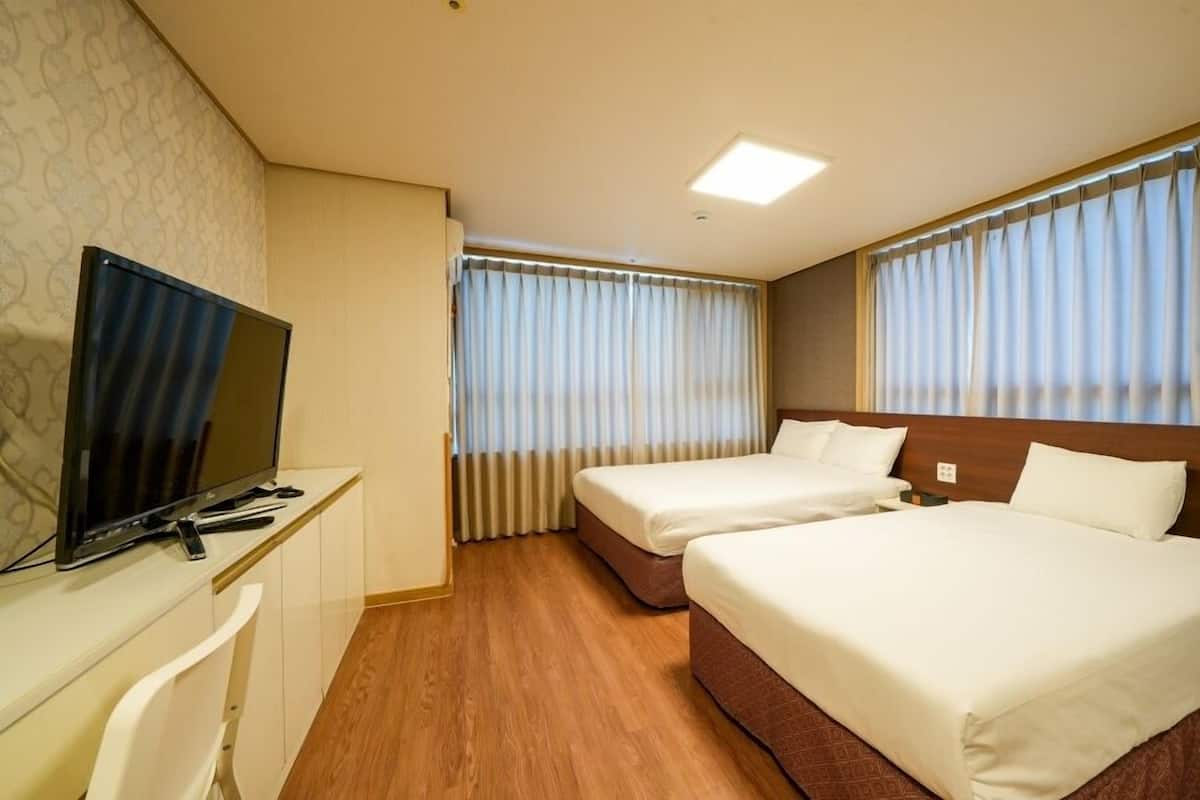 A hotel room with two beds, a TV, and a desk.