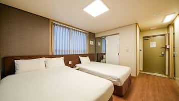 A hotel room with two beds, a large window with curtains, a mirror, and a door.
