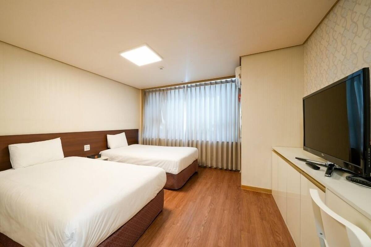 A hotel room with two beds, a TV, and a desk.