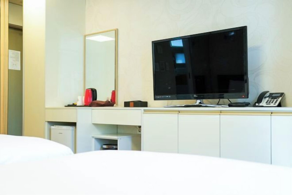 Quarto de hotel com cama, escrivaninha, computador, telefone e espelho.