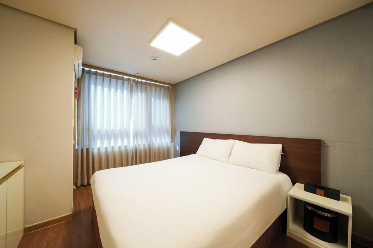 A hotel room with a large bed, a bedside table, a nightstand, and a window with curtains.