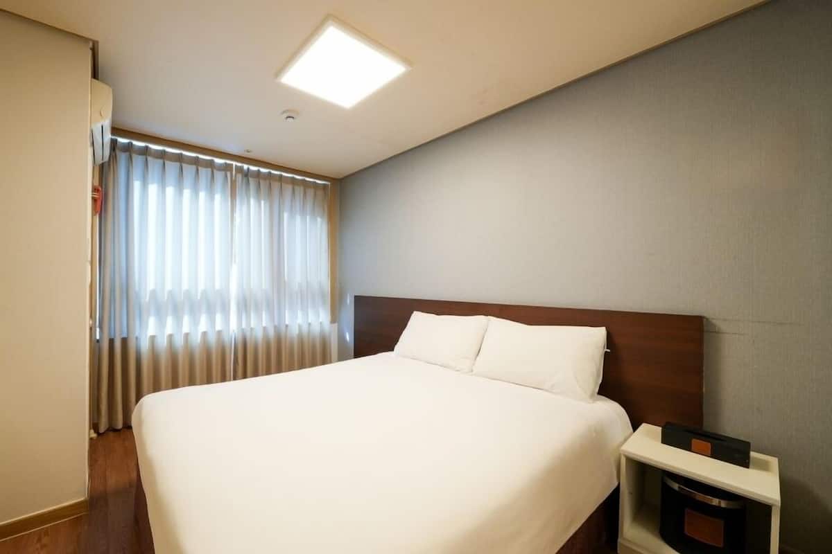 A hotel room with a large bed, a nightstand, a window with curtains, and a ceiling light.