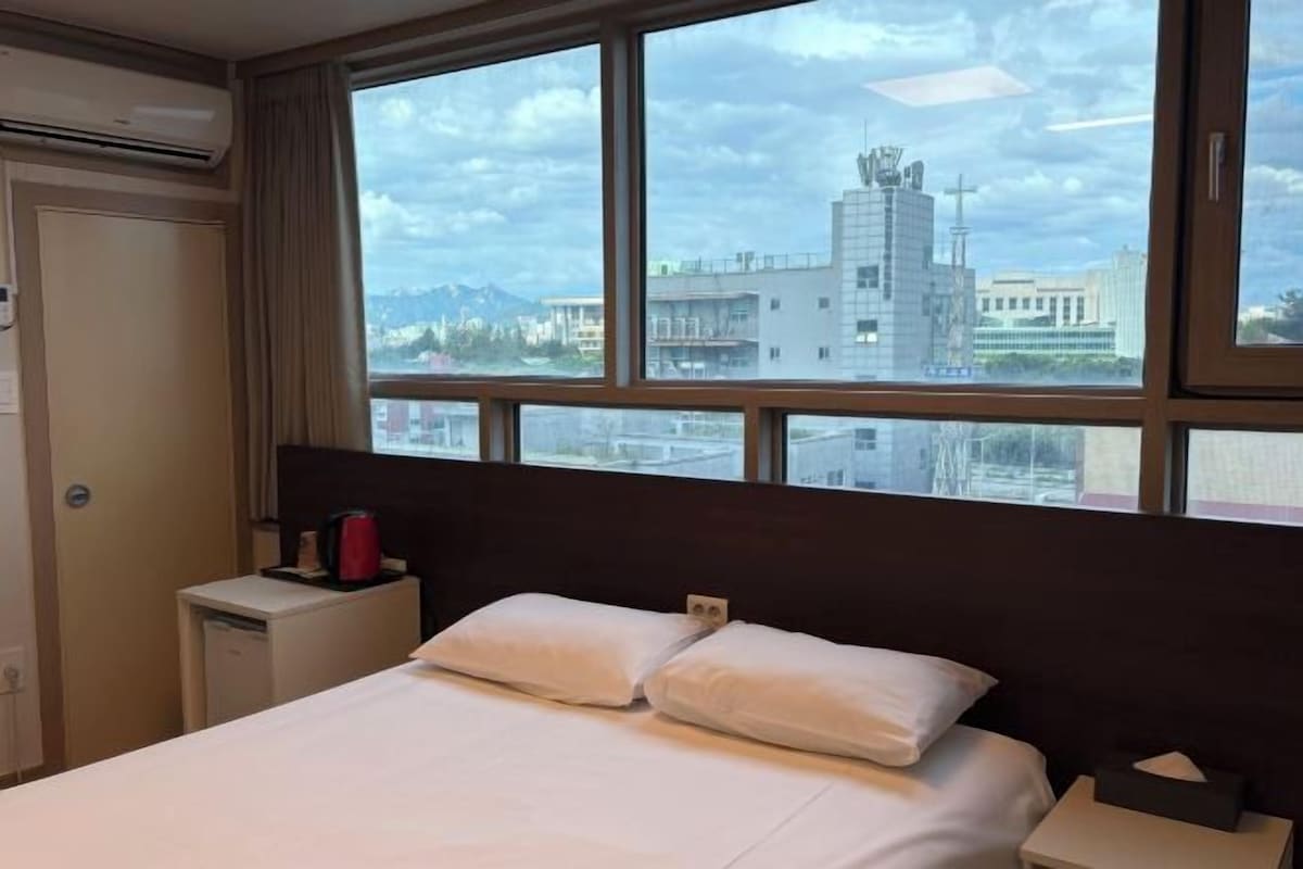 A hotel room with a bed, a nightstand, and a window with a city view.