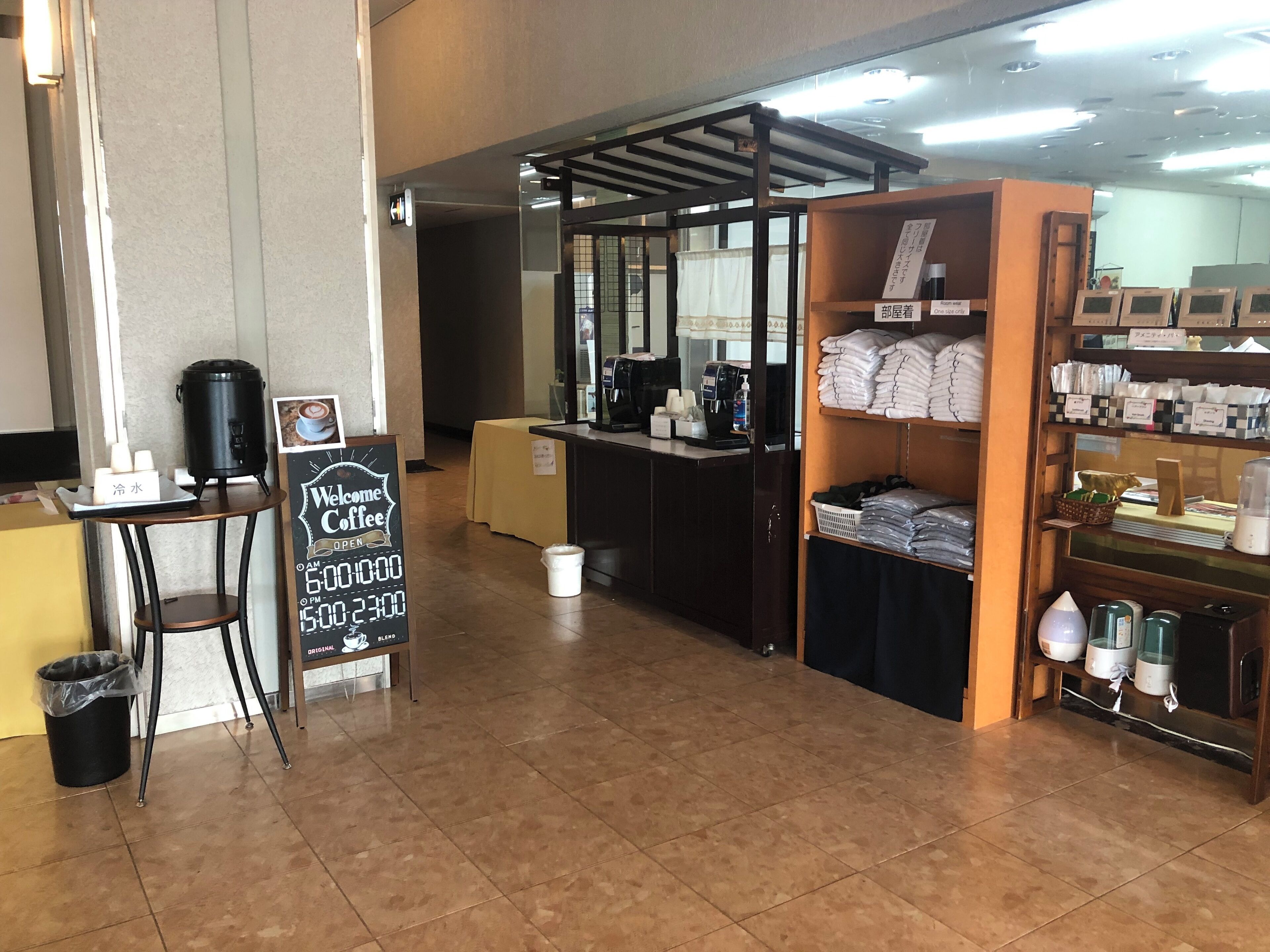 A coffee shop interior with a counter, a trash bin, a signboard, and shelves with packaged goods.