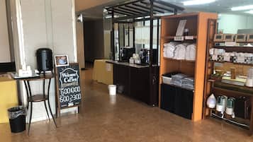A coffee shop interior with a counter, a trash bin, a signboard, and shelves with packaged goods.