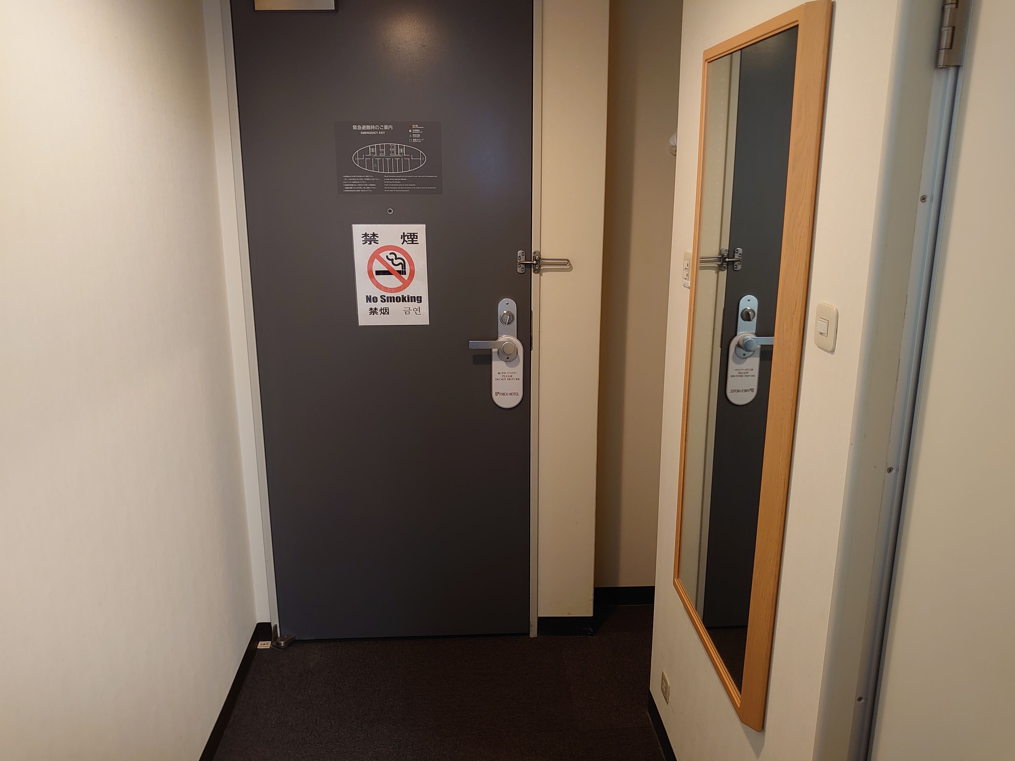 Porta di una camera d'hotel con cartello 'vietato fumare', mappa delle uscite di sicurezza e lettore di badge.