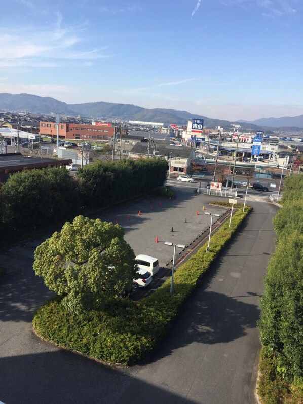 A parking lot with a white car, surrounded by greenery and buildings in the background.