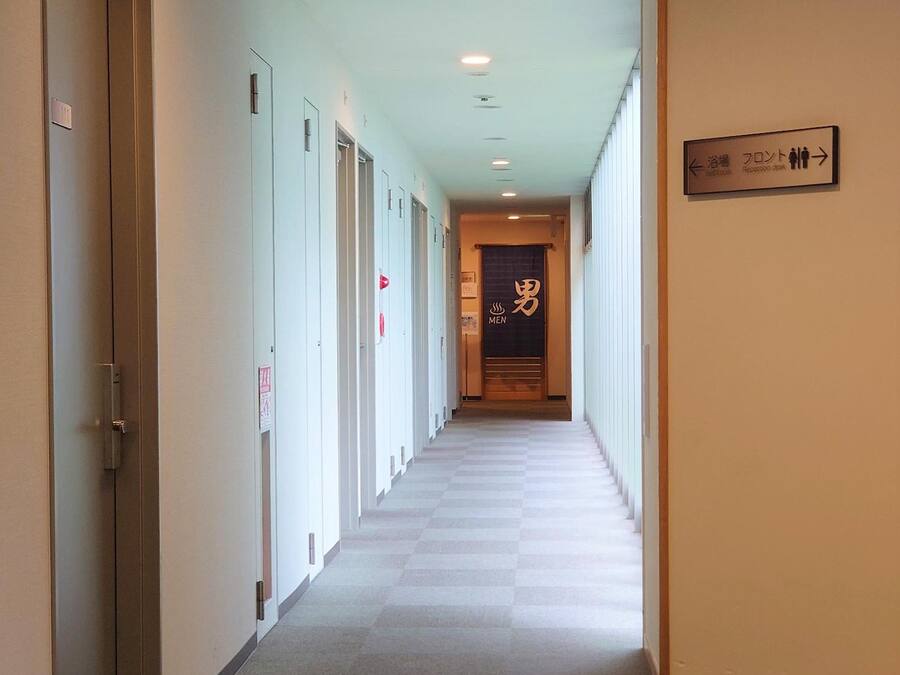 A hotel hallway with doors on both sides, a sign indicating a men's restroom, and a checkered floor.
