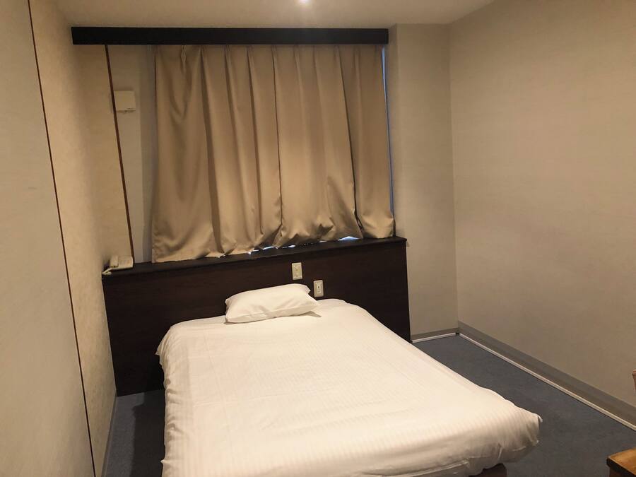 A small, neatly made bed in a room with a dark headboard and a window with curtains.
