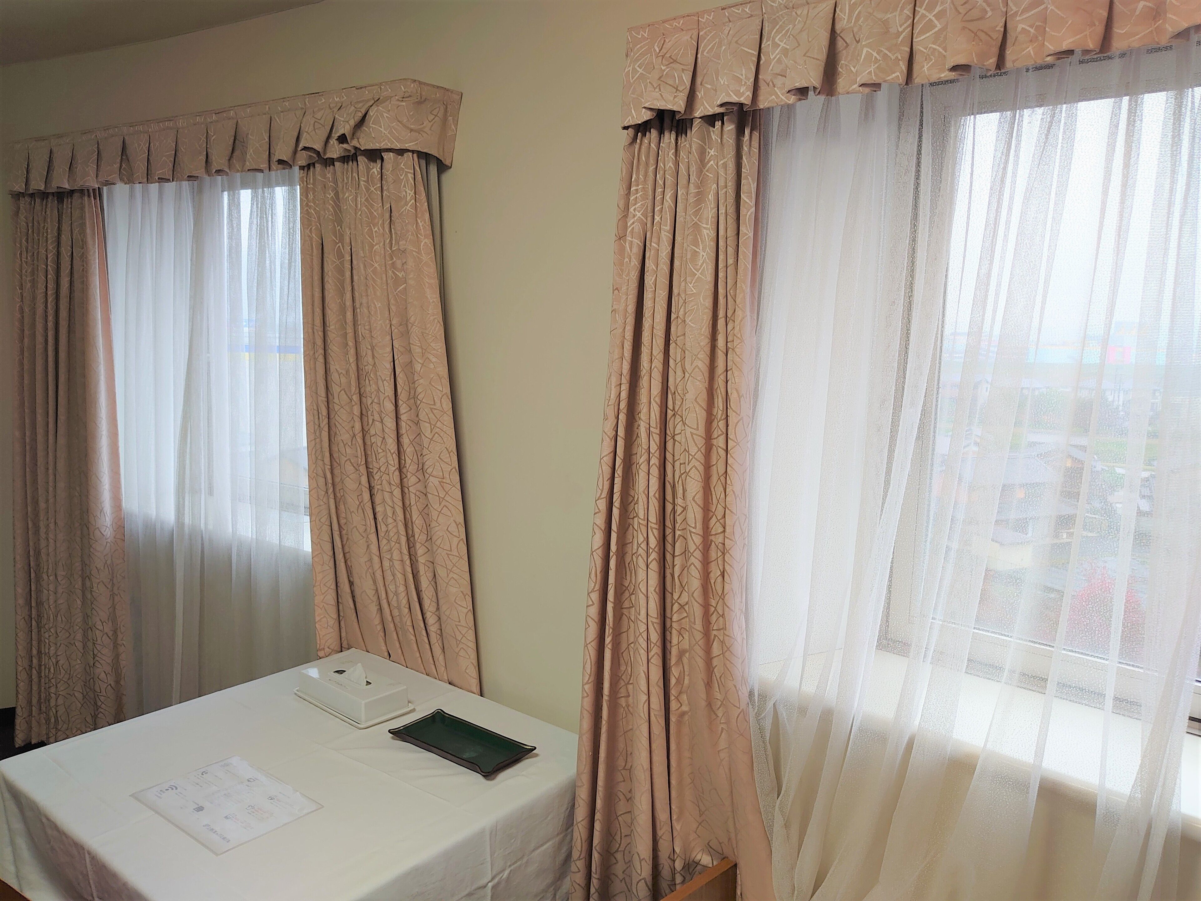 A hotel room with a bed, a table with a tissue box and a tray, and curtains with a pattern.