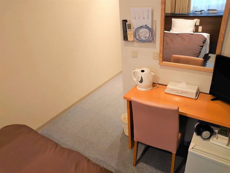 A hotel room with a bed, a desk with a kettle, a remote control, and a monitor.