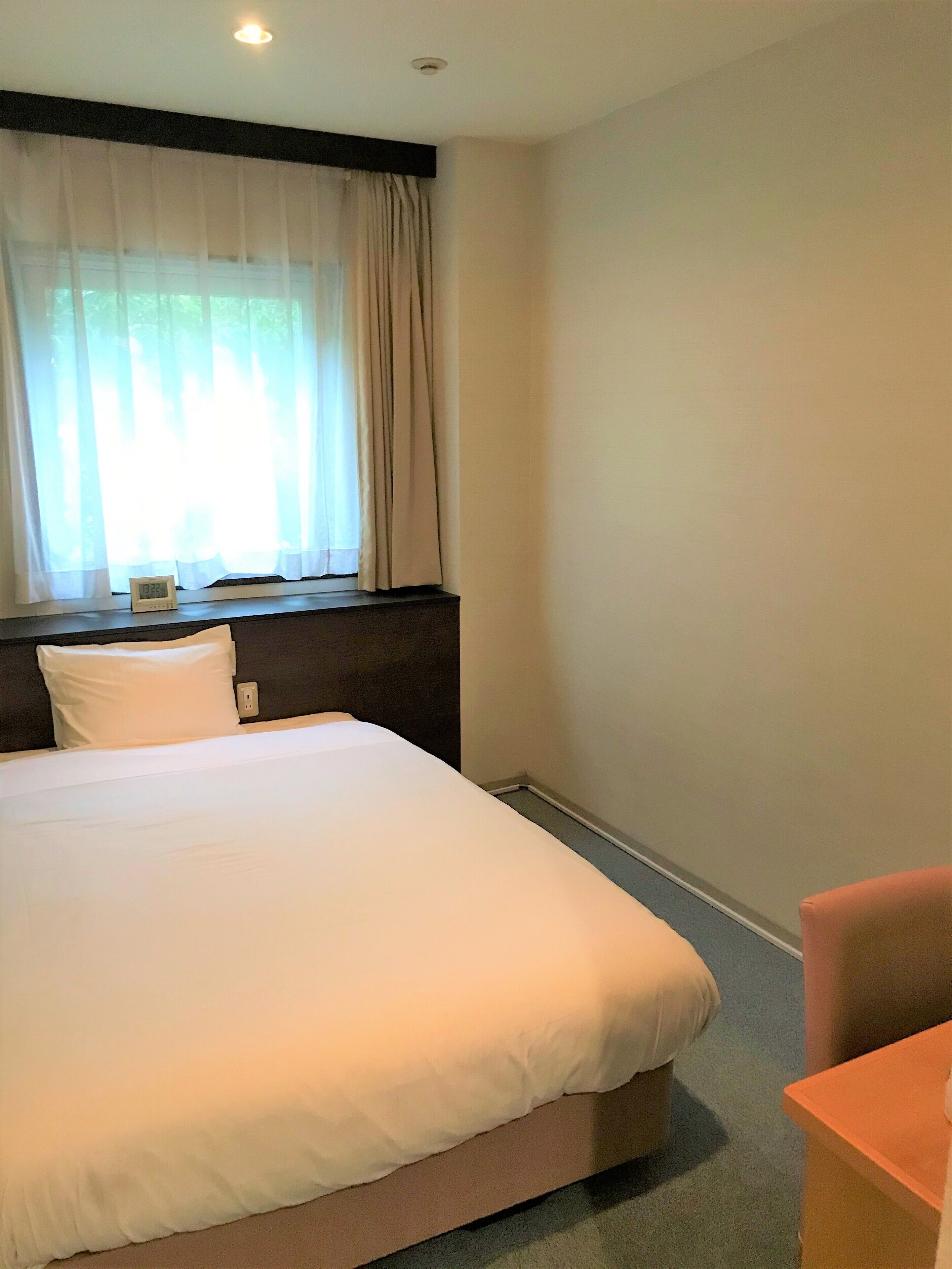A hotel room with a large bed, a nightstand, a chair, and a window with curtains.