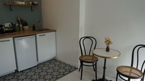 A compact kitchen with white cabinets, a wooden countertop, and a patterned rug. There are two wicker chairs and a small round table with a vase. - Spacious and Cosy Studio - Strasbourg Centre (Strasbourg)