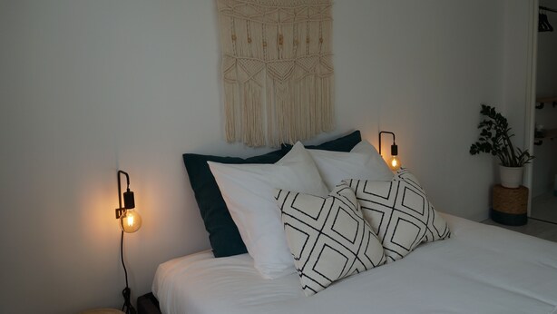 A bed with white and dark green pillows, a macrame wall hanging, and two wall-mounted lights. - Spacious and Cosy Studio - Strasbourg Centre (Strasbourg)