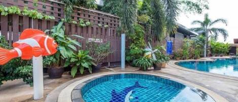 A swimming pool with a dolphin tile design, surrounded by potted plants and a wooden fence.