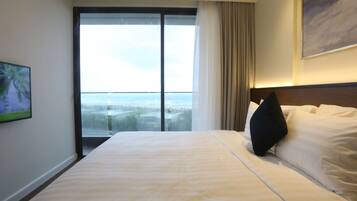 A hotel room with a large bed, a view through a glass door, and a painting on the wall.