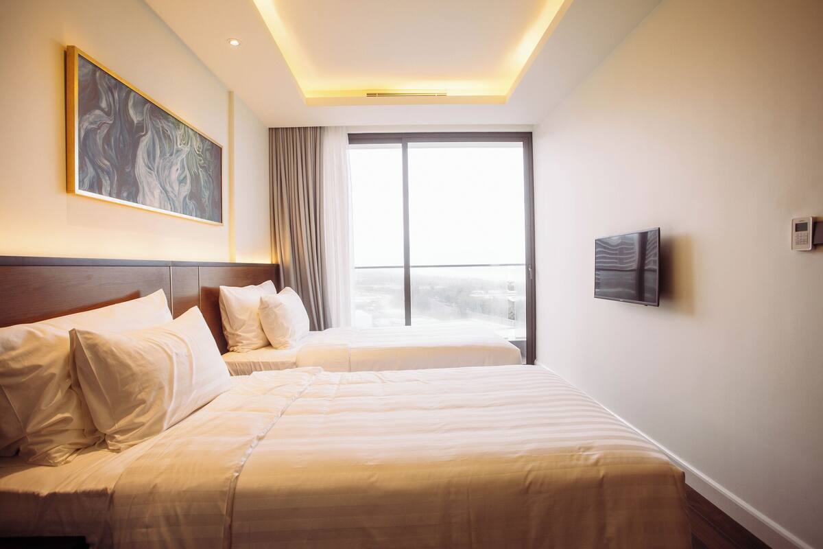 Ein Hotelzimmer mit zwei Betten, einem großen Fenster, einem Gemälde und einem Fernseher.