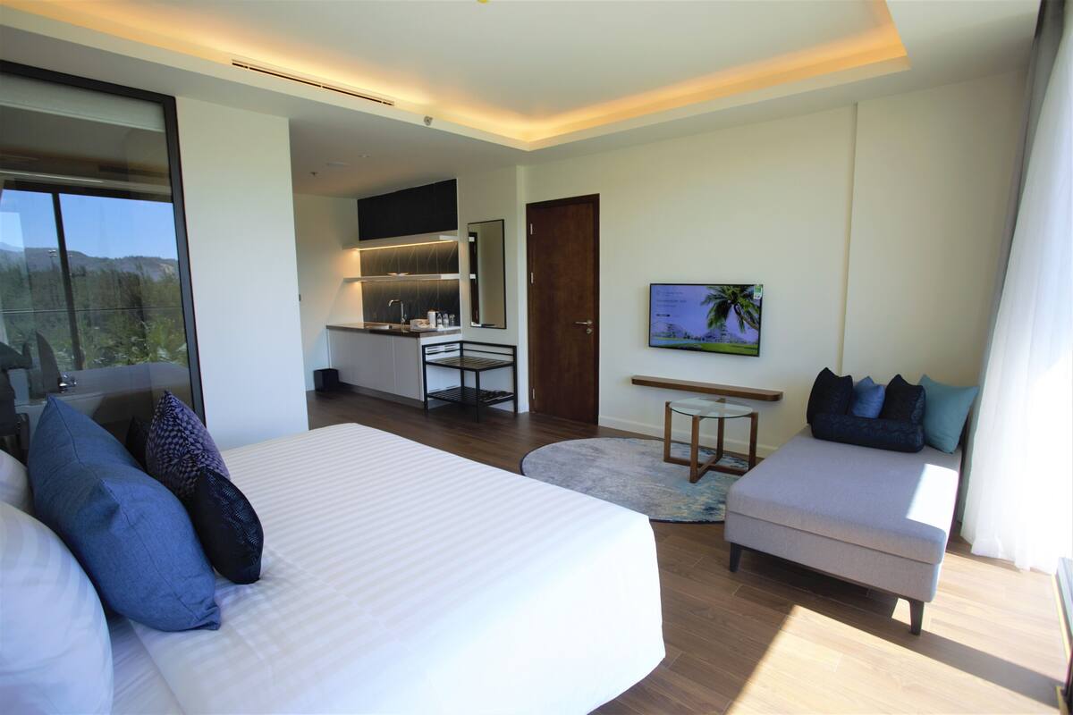 Ein modernes Hotelzimmer mit einem großen Bett, einer Couch, einem kleinen Tisch und einer Küchenzeile.