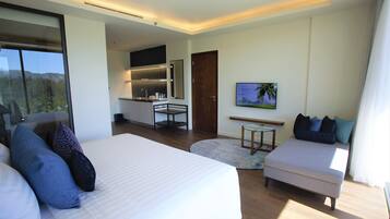 A modern hotel room with a large bed, a sofa, a small table, and a kitchen area.