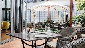 An outdoor dining area with tables and chairs, a large umbrella, and potted plants. - Altstadthotel Weinhaus Messerschmitt (Bamberg)