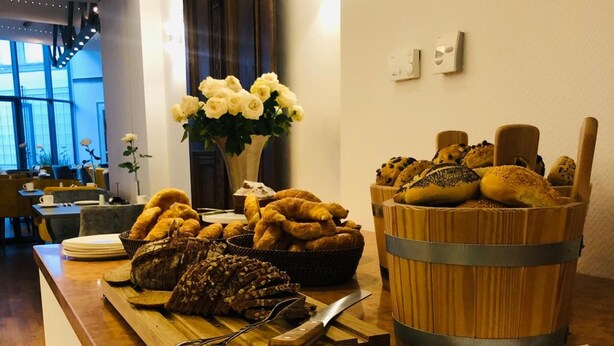 A breakfast buffet with pastries, bread, and a vase of flowers on a wooden counter. - Altstadthotel Weinhaus Messerschmitt (Bamberg)