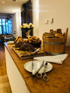 Een ontbijtbuffet met gebak, brood en een bloevas op een houten toonbank.