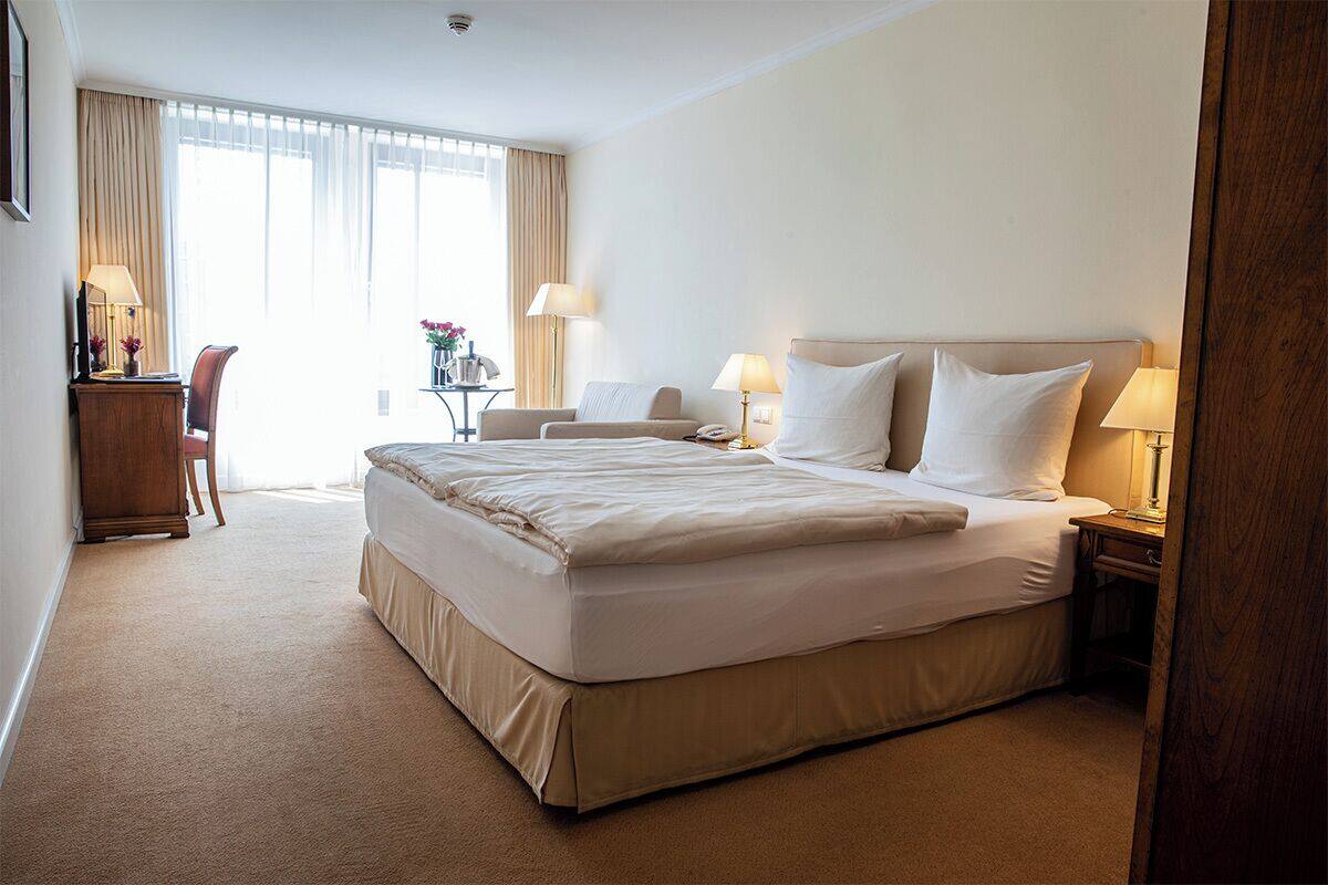 Ein Hotelzimmer mit einem großen Bett, Nachttischen, einem Schreibtisch und einem Sessel.