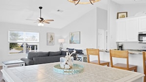 A modern living room with a sofa, dining table, and chairs. There is a ceiling fan, a kitchen area with cabinets, and artwork on the walls. - Beach house with ground floor mother in law suite! (Port St Joe)