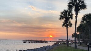 A sunset over a calm body of water with a pier extending into the water. Palm trees line the shore, and there is a grassy area with a pathway leading to a gazebo. - St Simons Island,  2 bedroom, 2 bath condo, short walk to village and beaches. (St. Simons)
