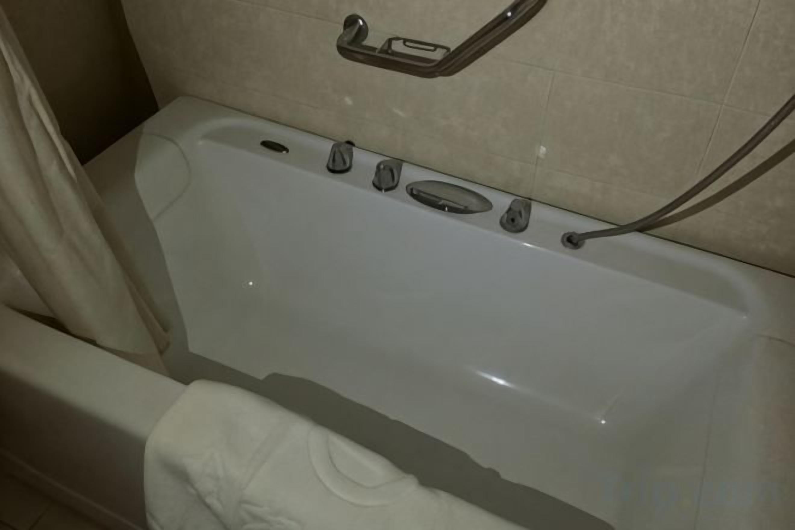 A bathtub with a shower curtain, a towel, and a grab bar on the wall.