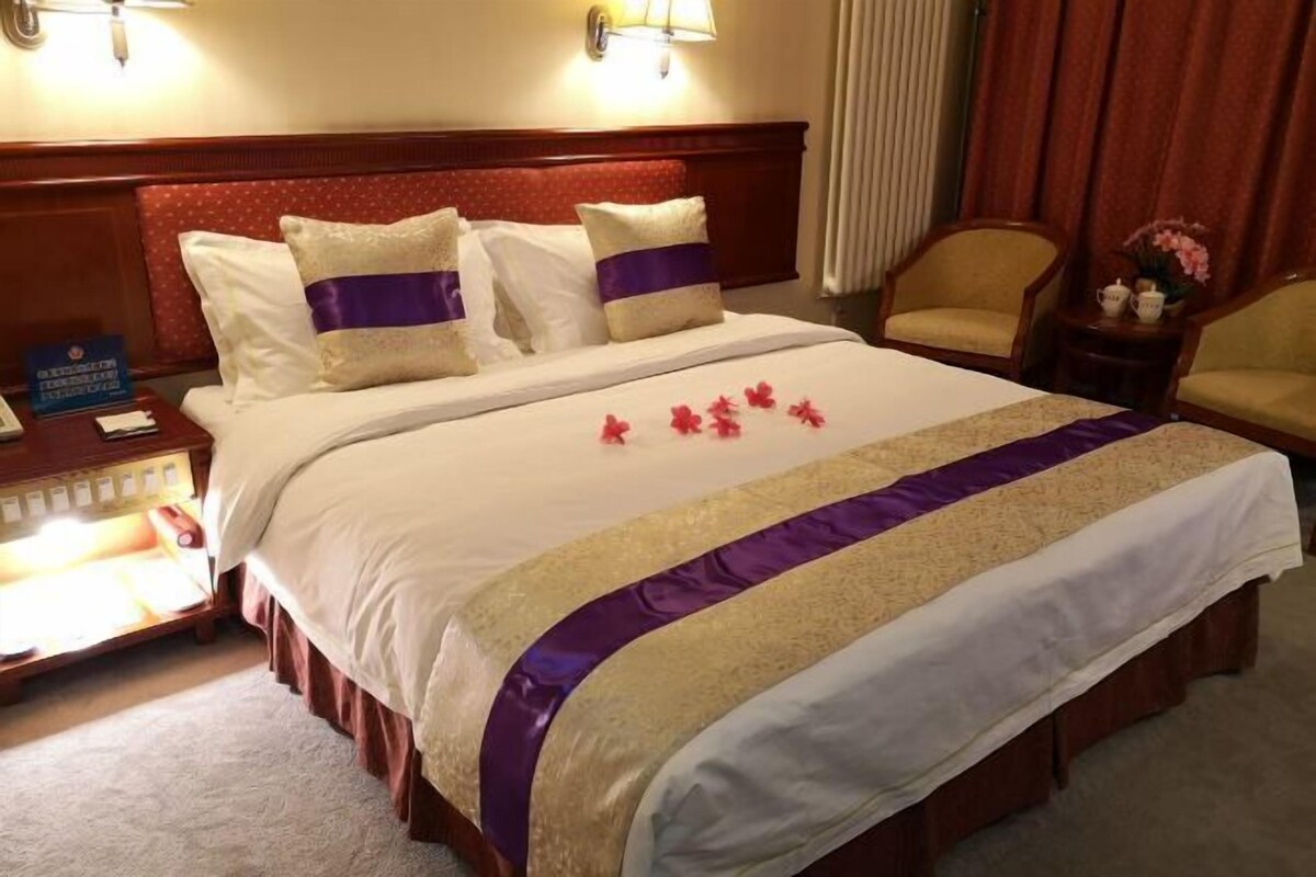 A hotel room with a large bed, two bedside lamps, a nightstand, a chair, and a small table with a vase of flowers.