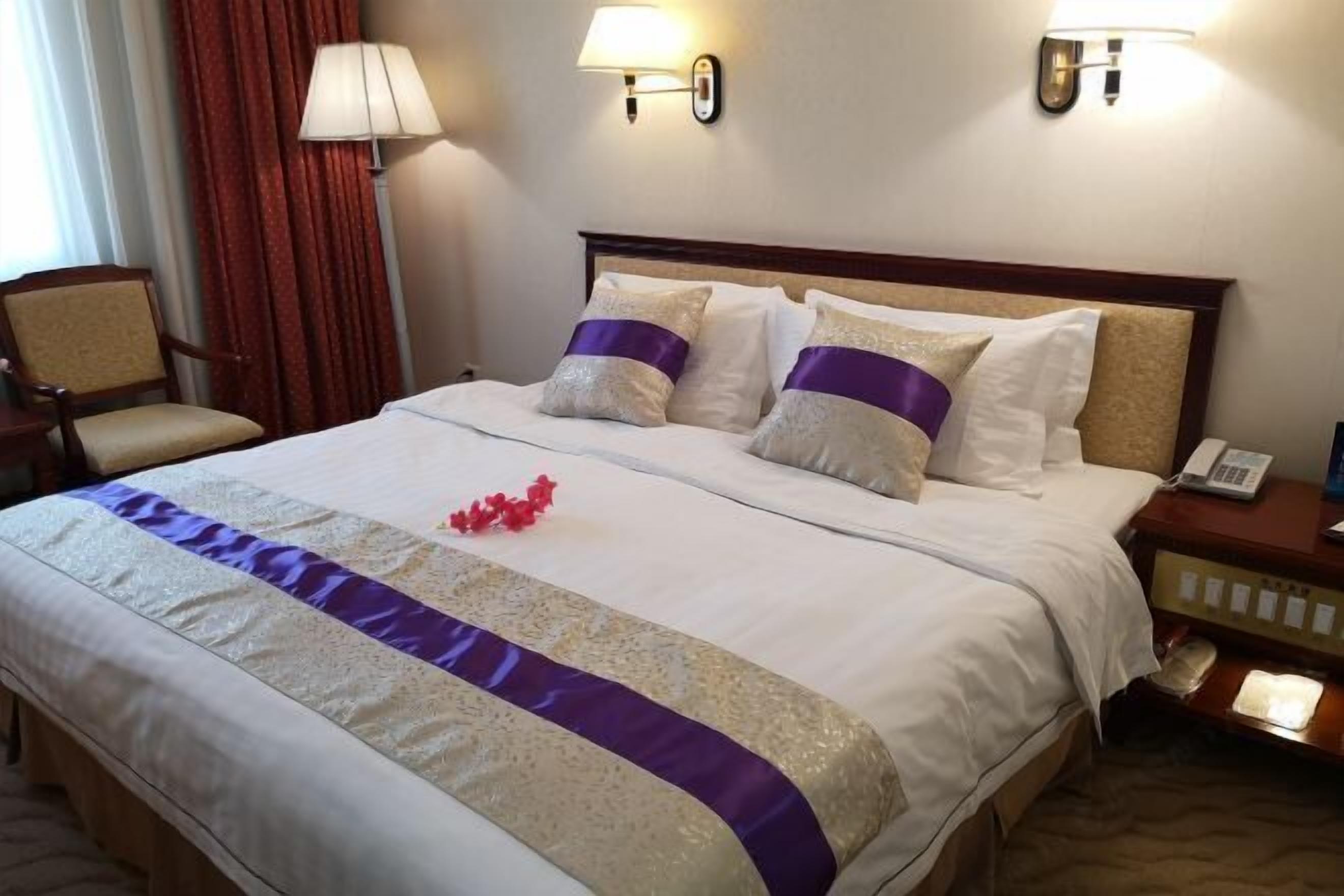 A hotel room with a large bed, two bedside lamps, a chair, and a nightstand with a phone.