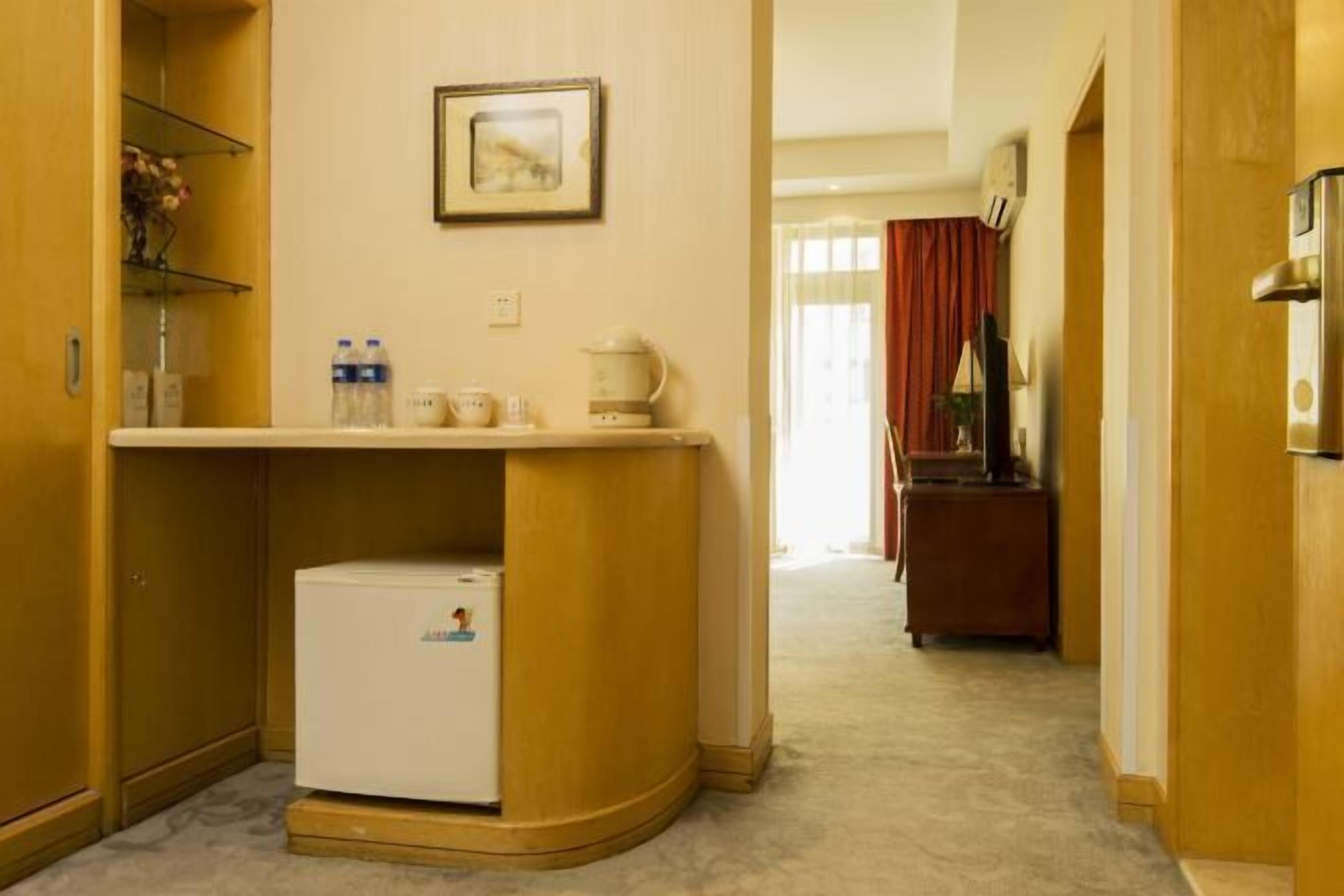 A compact hotel room with a kitchenette, a small refrigerator, a coffee maker, and a shelf with toiletries.