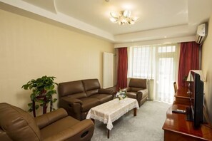 A living room with two brown leather sofas, a wooden coffee table with a lace tablecloth, a television on a wooden stand, and a potted plant. - Dong Fang Hotel (Beijing)