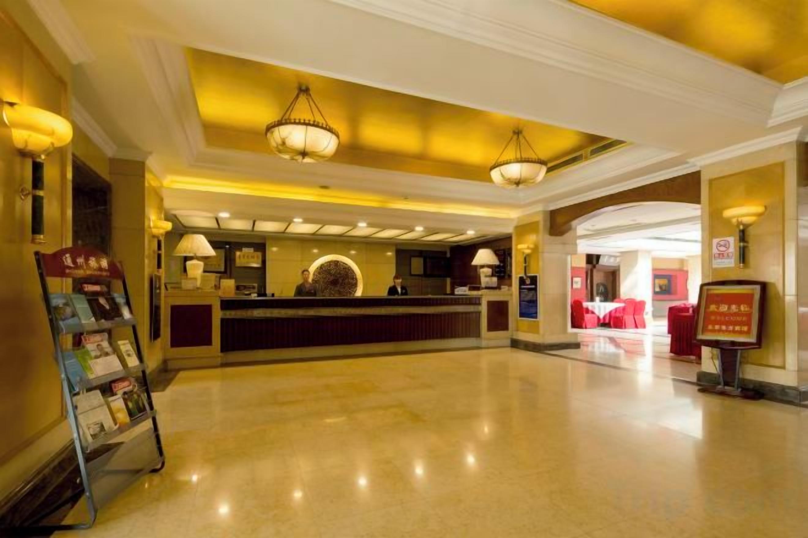A hotel lobby with a reception desk, chandeliers, and a clean, polished floor.