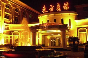 A hotel entrance with a fountain, illuminated signage, and a covered area. - Dong Fang Hotel (Beijing)