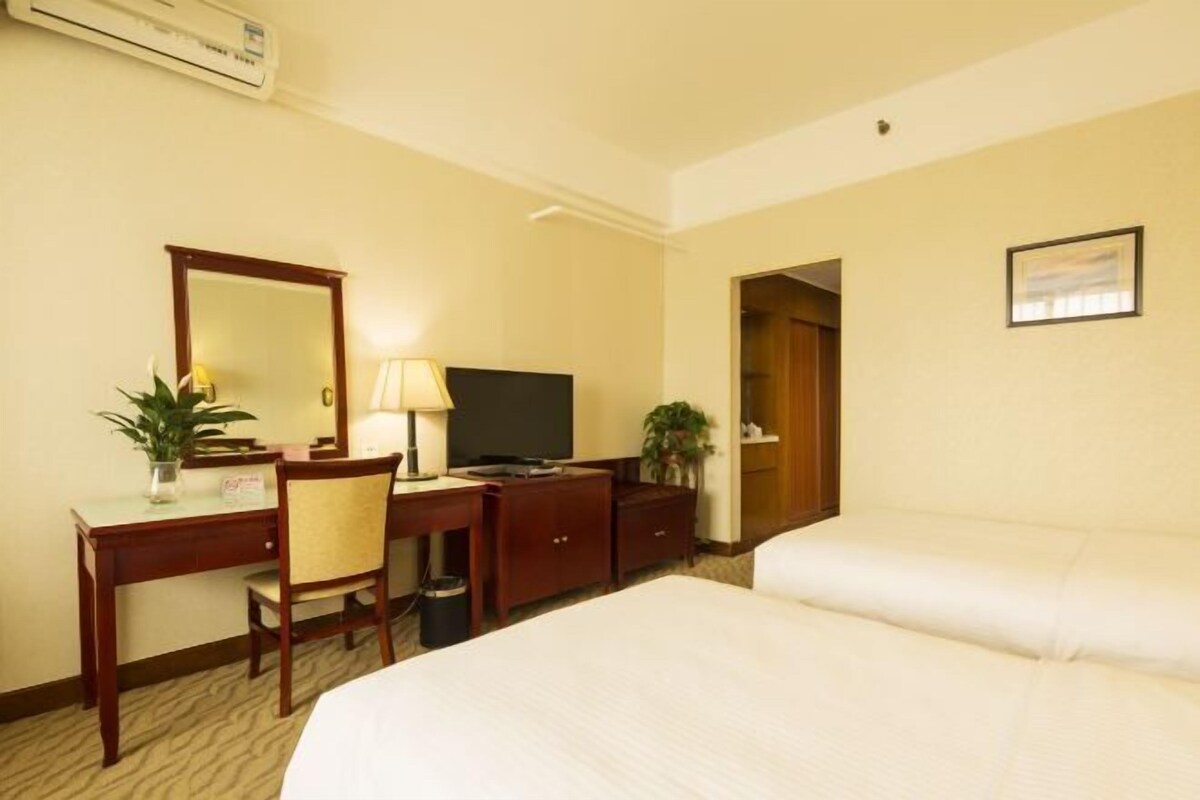 A hotel room with a bed, a desk with a chair, a television, and a mirror.