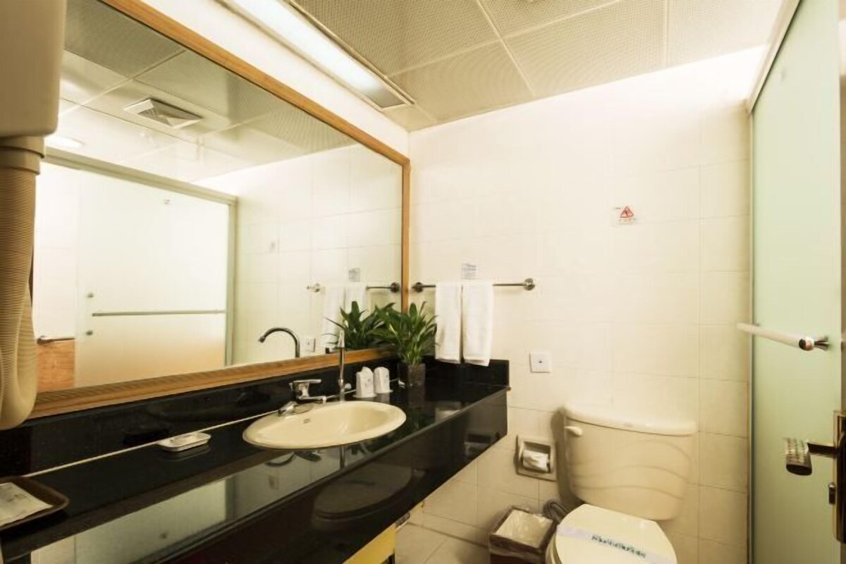 A modern bathroom with a black countertop, a white sink, a mirror, and a toilet.
