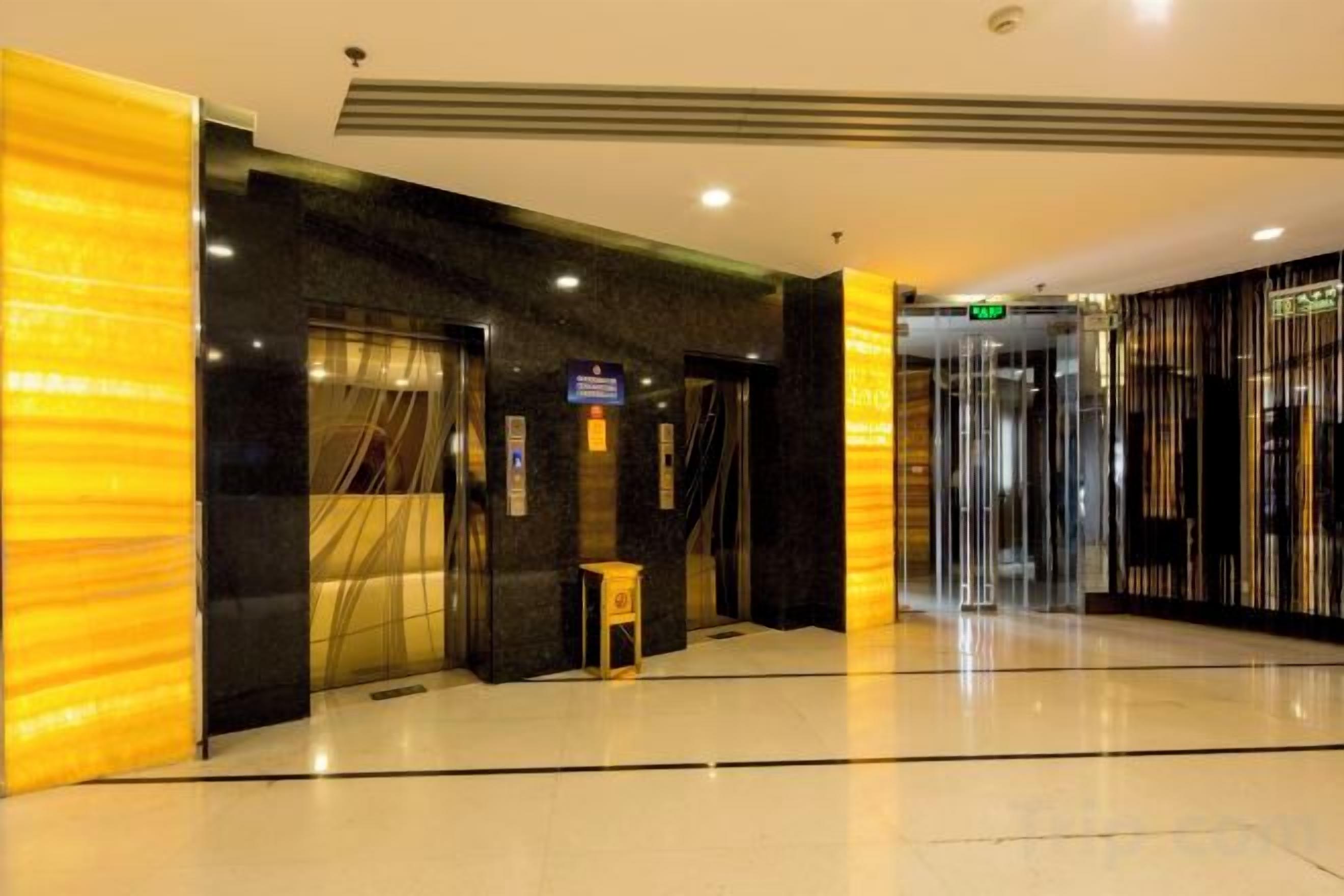 A hotel lobby with a modern design, featuring a marble floor, a reception desk, and a glass elevator.