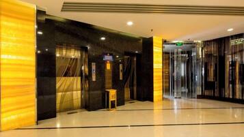 A hotel lobby with a modern design, featuring a marble floor, a reception desk, and a glass elevator.