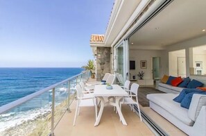 Ein Balkon mit einem weißen Tisch und Stühlen, einer Couch mit bunten Kissen und Meerblick.