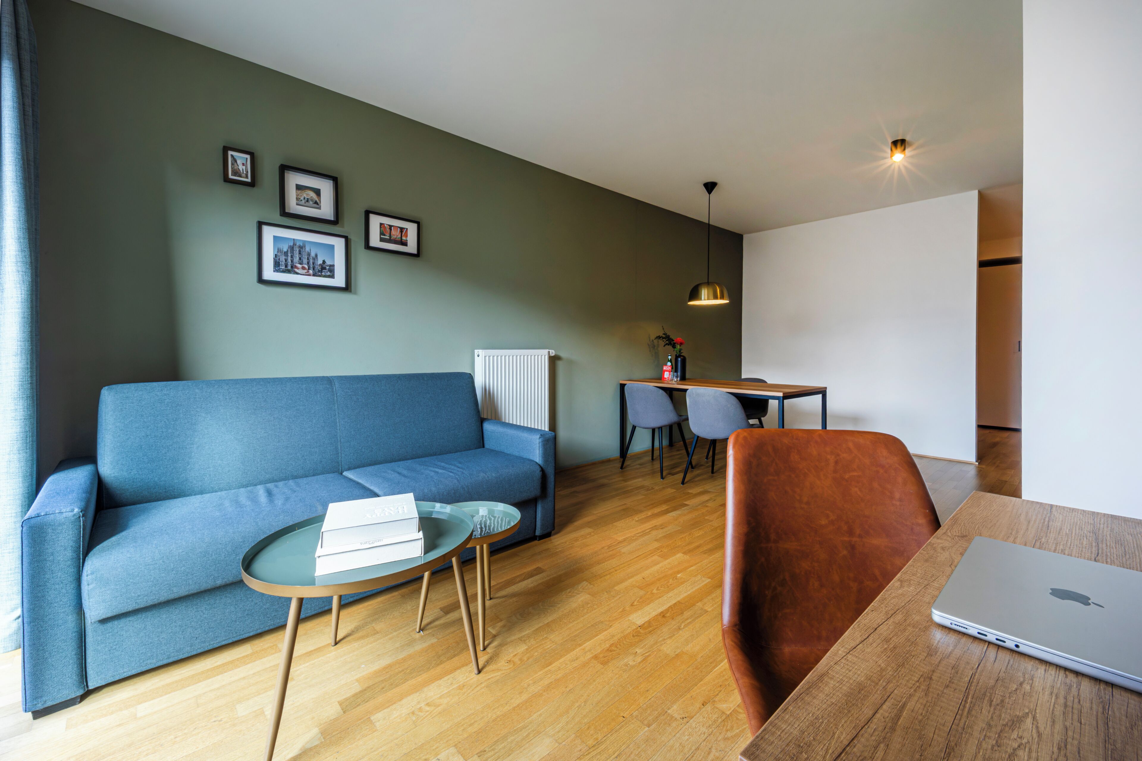 Een moderne woonkamer met een blauwe bank, een ronde salontafel, een houten eettafel en een laptop.