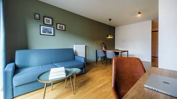 Een moderne woonkamer met een blauwe bank, een ronde salontafel, een houten eettafel en een laptop.