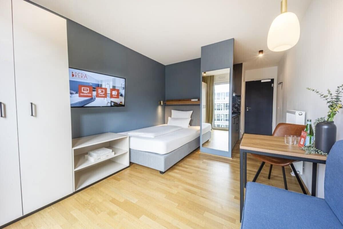 Una habitación de hotel moderna con una cama, un escritorio, una silla, un televisor y un ventanal grande.
