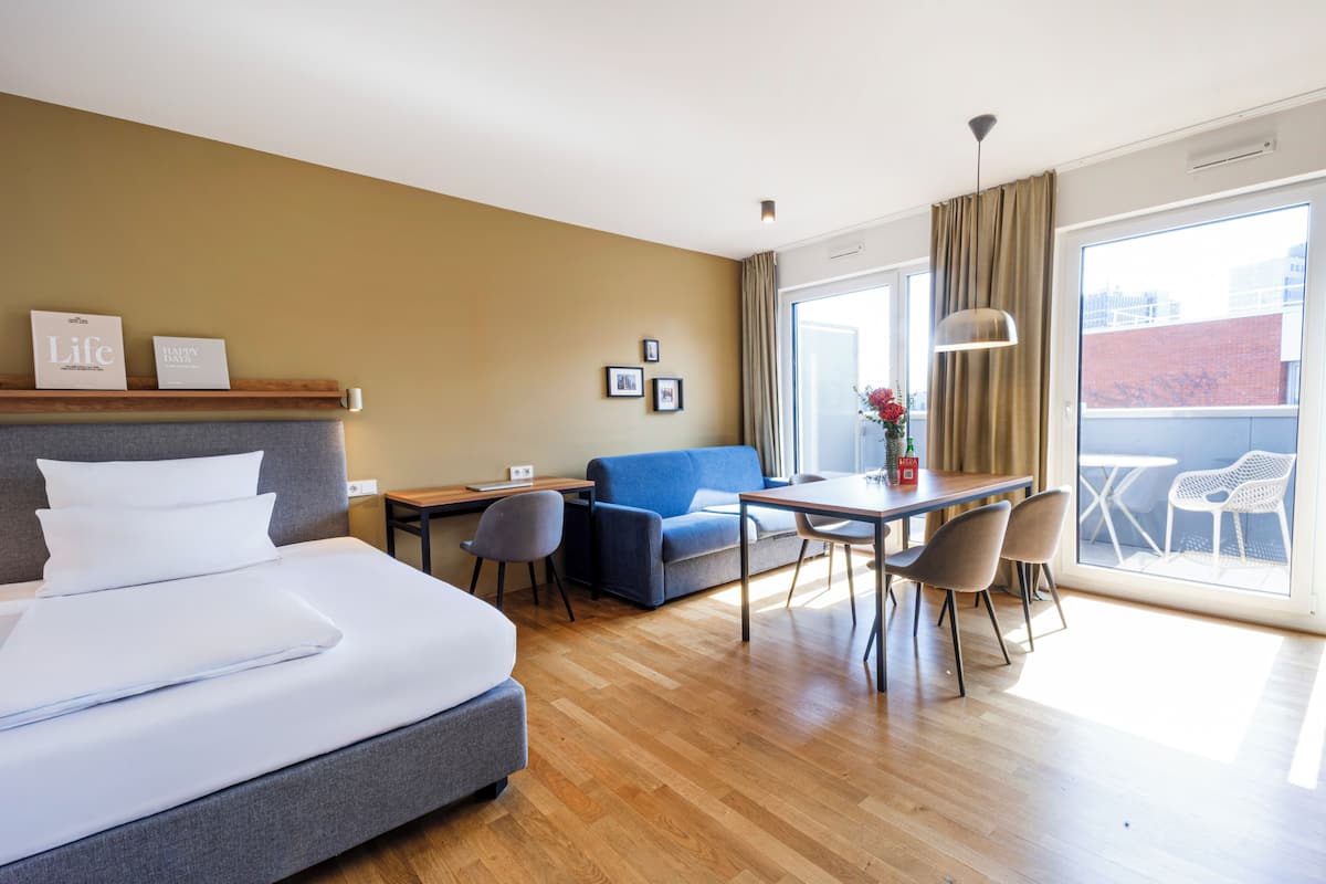 Habitación de hotel con cama, escritorio, sofá y balcón con sillas.