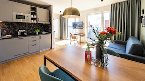Uma cozinha moderna com micro-ondas embutido, uma sala de jantar com mesa e cadeiras de madeira, e uma sala de estar com sofá e televisão.